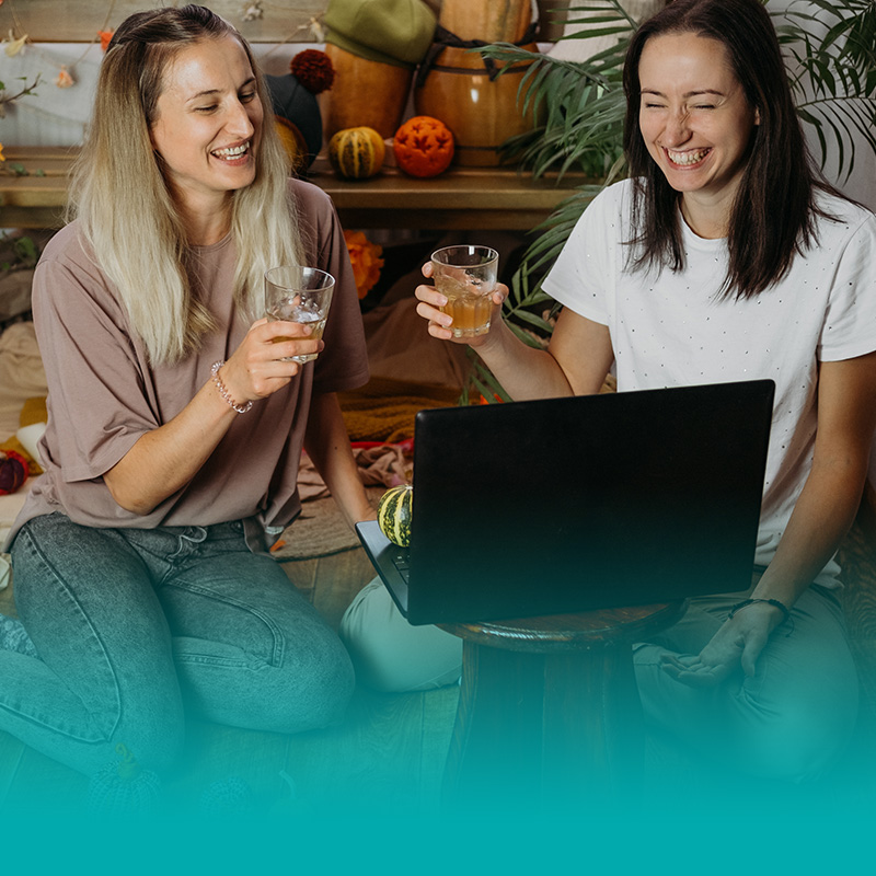 Photo of two women with drinking glasses in front of a computer
